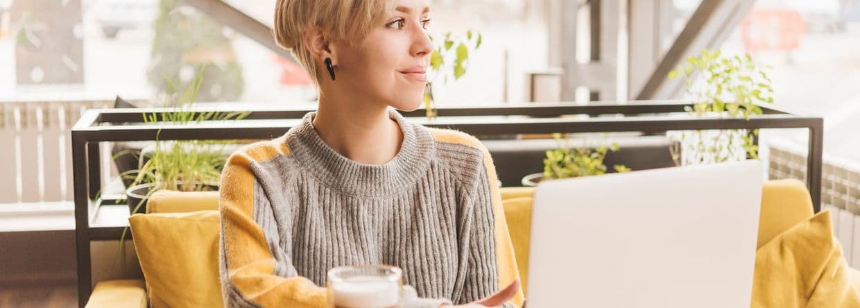 A girl working on a computer sitting at a table with a coffe mug