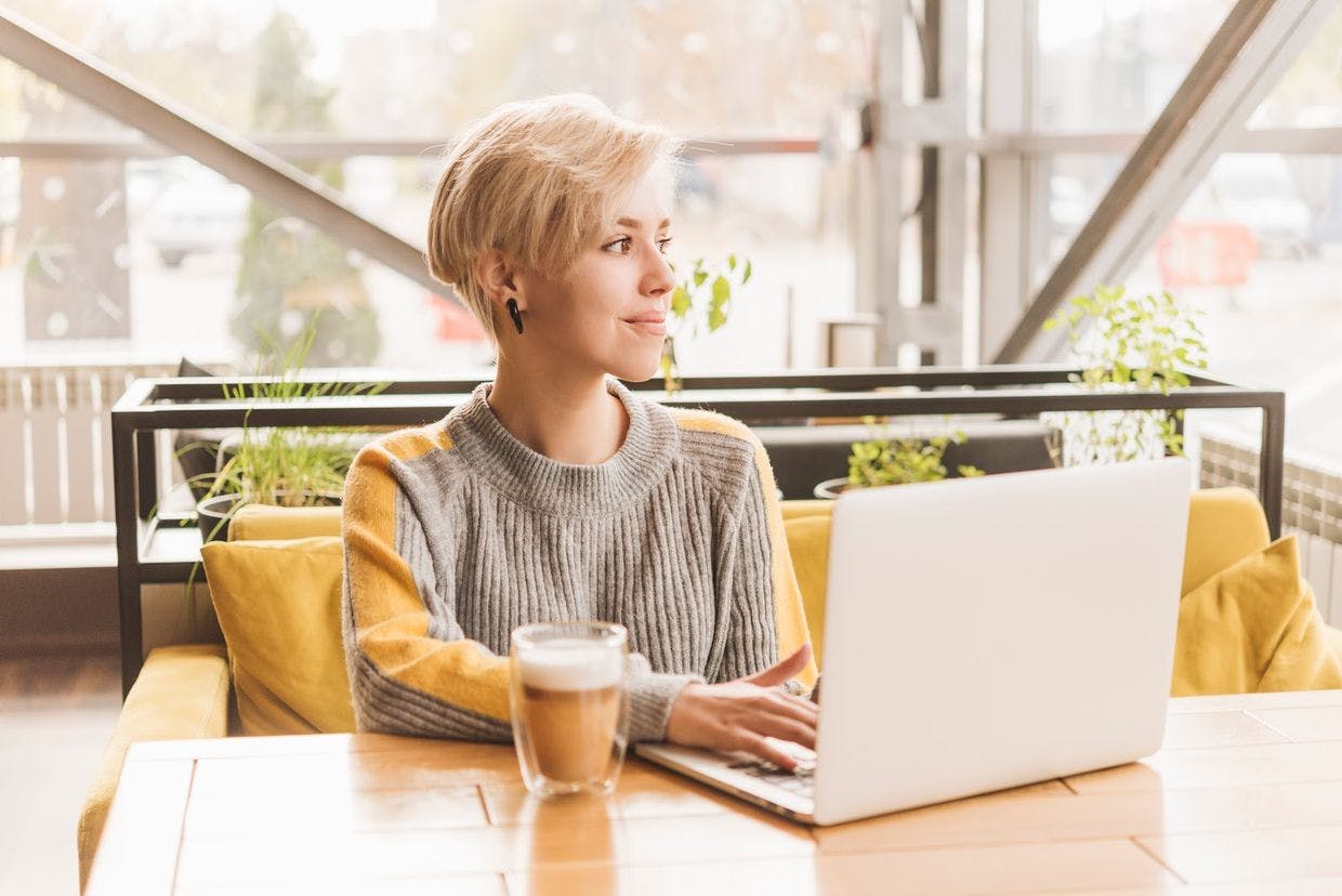 A girl working on a computer sitting at a table with a coffe mug